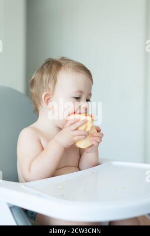 Bébé mangeant une pomme assis sur une chaise haute Banque D'Images