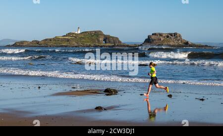 East Lothian, Écosse, Royaume-Uni, 27 septembre 2020. Scurry Running Event : les coureurs participent à un événement de course amusant de la plage de Yellowcraig à North Berwick et de retour sur une belle matinée ensoleillée d'automne. Fidra Island est à l'arrière-plan tandis qu'une femelle court sur la plage avec reflété dans le sable humide Banque D'Images