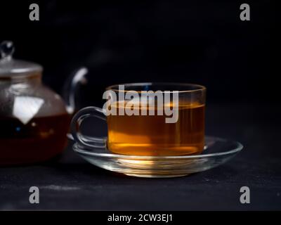 Une tasse de thé chaud fraîchement préparé et une théière sur la table avec un fond noir. Banque D'Images