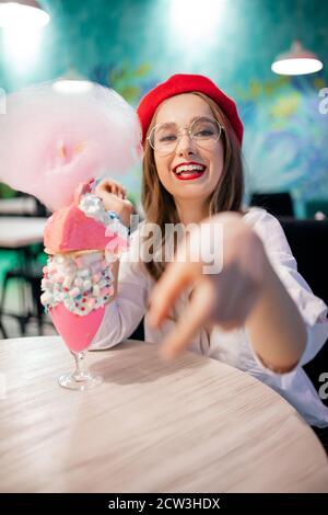 France doux dessert national, fille en béret rouge mange gâteau rose, bonbons floss et milkshake, rire et sourires Banque D'Images