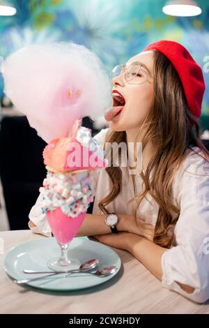 Dessert sucré avec bonbons en coton rose, milkshake et gâteau. Fille en béret rouge et verres, café en France Banque D'Images