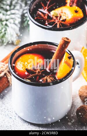 Vin chaud dans des mugs en métal blanc à la cannelle, aux épices et à l'orange sur fond gris, boisson traditionnelle pendant les vacances d'hiver. Sous la neige Banque D'Images