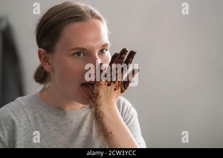 fille gaie léchant le chocolat de ses mains après avoir fait des bonbons, peu profond foyer Banque D'Images