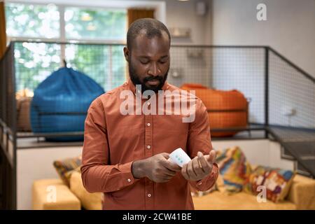 Jeune travailleur de bureau africain vérifiant la température avec thermomètre infrarouge pendant dans un bureau moderne Banque D'Images