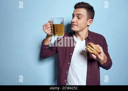 homme gai ivre avec une tasse de bière et un hamburger à la main régime alimentaire style de vie fond bleu Banque D'Images