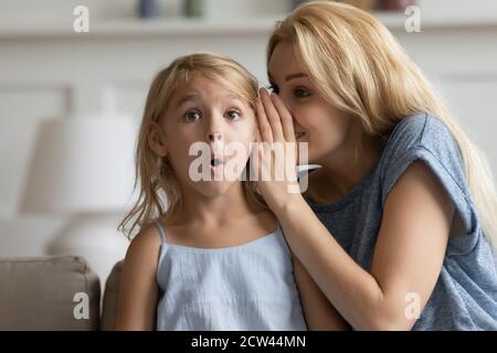 Une mère souriante dit le secret à l'oreille de sa petite fille Banque D'Images