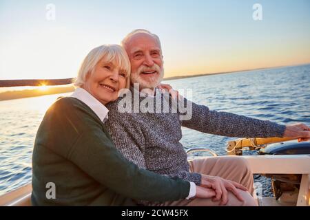 Portrait d'un beau couple senior souriant tenant les mains, se tenant et se relaxant ensemble tout en étant assis sur le côté du voilier ou du yacht flottant à l'intérieur Banque D'Images