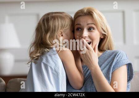 Naughty préscolaire fille chuchotant blague sur l'oreille de soeur émervetée Banque D'Images