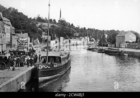 Une vue historique des quais pris de l'ancien pont de Dinan avec un bateau à côté des excursions publicitaires à l'Hôtel de l'Univers à Saint Malo en aval. À Denin, Côtes-d'Armor, Bretagne, France, tiré d'une carte postale vers 1900s. Banque D'Images