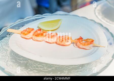 Brochettes de crevettes grillées servies avec une tranche de citron sur une assiette blanche. Festival de la cuisine de rue. Style fruits de mer Banque D'Images