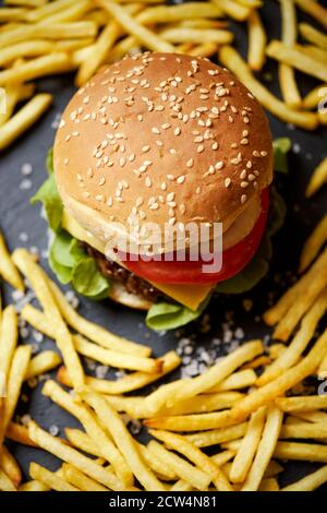 cheeseburger entouré de frites sur une table noire Banque D'Images
