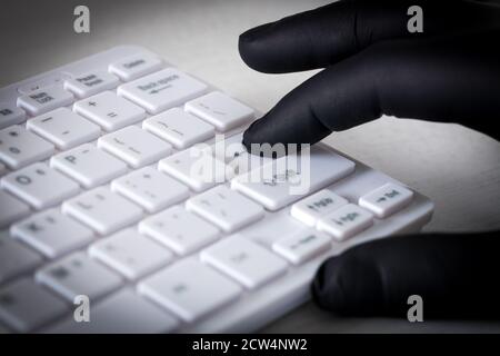 Clavier d'ordinateur blanc et mains dans des gants en caoutchouc noir. Concept de crime et de harcèlement sur le Web Banque D'Images