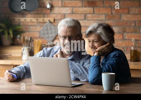 Un homme et une femme heureux et âgés utilisent un ordinateur portable à la maison ensemble Banque D'Images