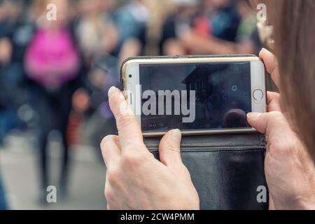 Image des mains de femmes tenant un téléphone mobile qui tourne un spectacle dans la rue Banque D'Images