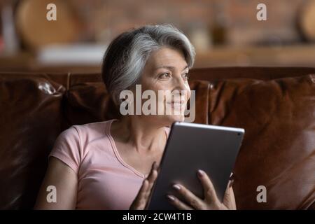 Une femme âgée souriante utilise une tablette pour se détendre à la maison Banque D'Images