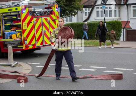 Une pompier lance le tuyau avec la brigade de pompiers de Londres pour assister à un incendie de maison dans une rue résidentielle, sud de Londres, Angleterre, Royaume-Uni Banque D'Images