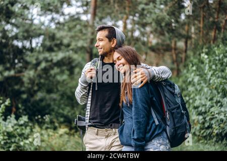 Jeune couple avec des sacs à dos sur le dos souriant et marchant dans la forêt, profiter de la promenade. Banque D'Images