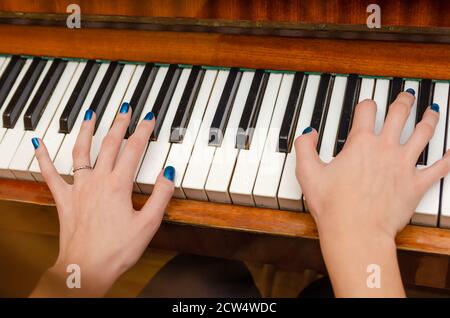 Mains d'une pianiste féminine avec vernis à ongles bleu sur les ongles sur les clés d'un piano. Fille jouant le piano. Banque D'Images