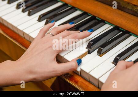 Mains d'une pianiste féminine avec vernis à ongles bleu sur les ongles sur les clés d'un piano. Fille jouant le piano. Banque D'Images