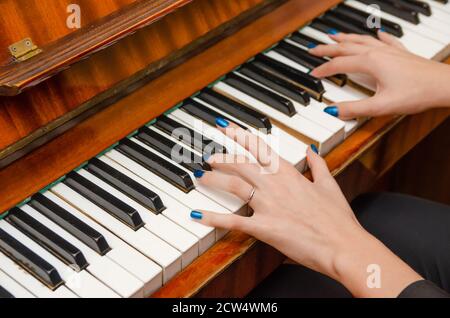 Mains d'une pianiste féminine avec vernis à ongles bleu sur les ongles sur les clés d'un piano. Fille jouant le piano. Banque D'Images