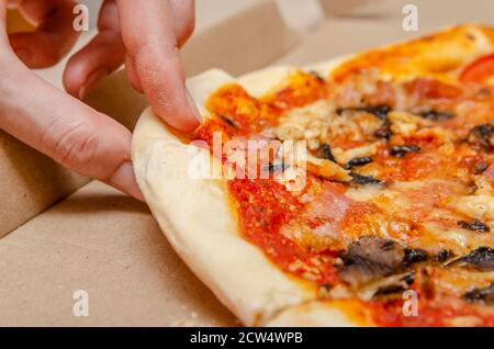 La main femelle prend une pizza à la viande avec des champignons d'un simple boîte en carton en gros plan Banque D'Images