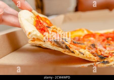 La main femelle prend une pizza à la viande avec des champignons d'un simple boîte en carton en gros plan Banque D'Images