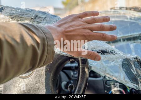 Un homme se frapette contre le pare-brise cassé. Fissures sur le pare-brise de la voiture dues à l'impact Banque D'Images