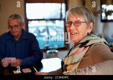 Portrait d'un couple senior souriant à la maison assis à la table Jouer les cartes ensemble Banque D'Images