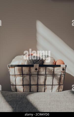 Panier de skeins de couleur terre de fil à l'intérieur d'un appartement, contre un mur, lumière du soleil de la fenêtre sur lui, foyer sélectif. Banque D'Images