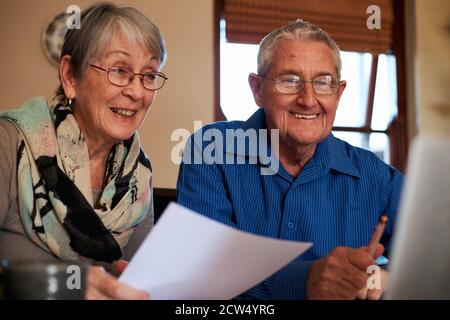 Un couple senior souriant à la maison vérifie les finances personnelles sur un ordinateur portable Banque D'Images