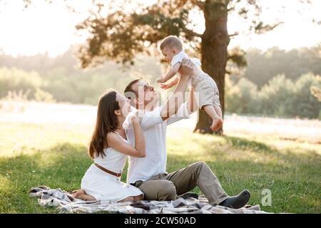 maman, papa lève son bébé garçon en plein air et regarde son sourire. Parents heureux de passer du temps à jouer avec son fils dans le parc le jour de l'été. Sélectif Banque D'Images