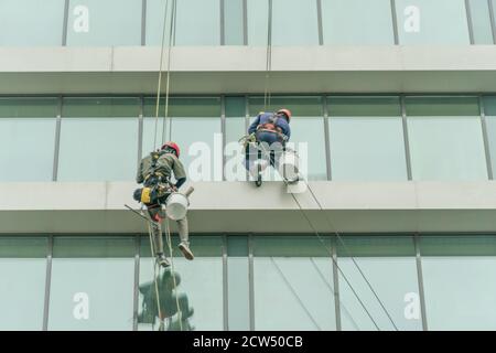 Deux travailleurs lavent les fenêtres d'un bâtiment en verre de grande hauteur. Travail en hauteur, alpinisme industriel Banque D'Images