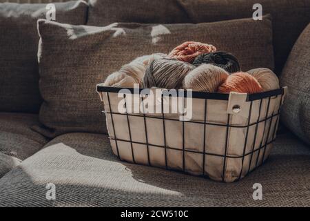 Panier de skeins de couleur terre de fil sur un canapé, lumière du soleil de la fenêtre dessus, foyer sélectif. Banque D'Images