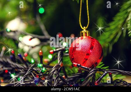 Gros plan - le ballon de Noël rouge suspendu sur l'arbre de Noël parmi les lumières de Noël. Magnifique Noël et nouvel an Banque D'Images