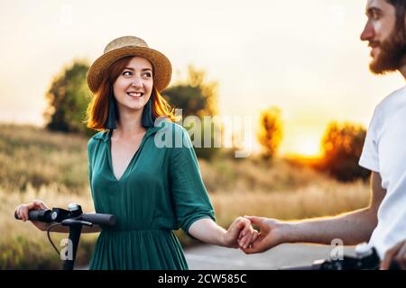 Homme et femme tenant les mains. Sur la route de fond et le coucher du soleil. Marche sur des scooters électriques. Banque D'Images