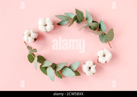 Composition florale, couronne en branches d'eucalyptus, feuilles et coton isolée sur fond rose. Plan plat, vue du dessus. Concept floral Banque D'Images