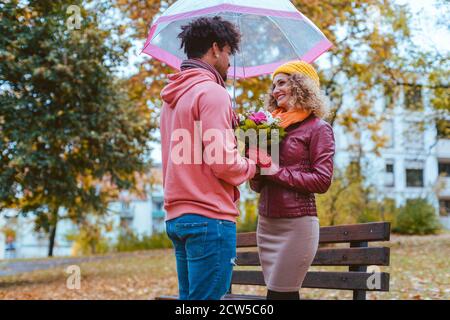 Homme noir donnant des fleurs pour sa petite amie de race blanche à l'automne Banque D'Images