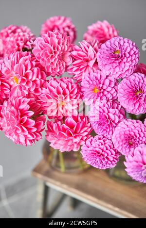 Dahlias lilas et roses dans un pot en verre, sur fond de mur neutre. Le travail du fleuriste dans un fleuriste. Joli bouquet frais. Livraison de fleurs Banque D'Images