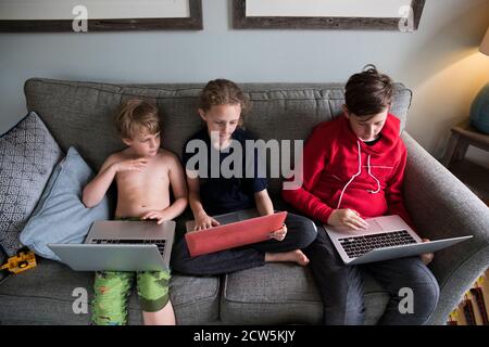 Trois frères et sœurs travaillent ensemble sur des ordinateurs portables pour l'apprentissage virtuel Banque D'Images