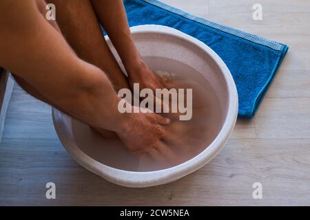 Un homme met les mains et les pieds dans le bain avec de l'eau chaude et du bicarbonate de soude à la maison. Banque D'Images
