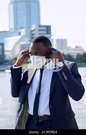 Jeune homme d'affaires africain en vêtements de formal mettant sur le masque de protection à l'extérieur Banque D'Images