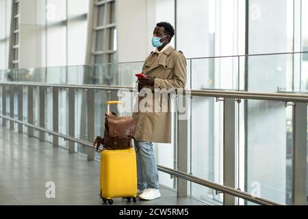 Voyageur afro-américain avec des stands de valise jaunes dans le terminal de l'aéroport, porter un masque de protection pour se protéger contre le virus de la grippe, pandémie COV Banque D'Images