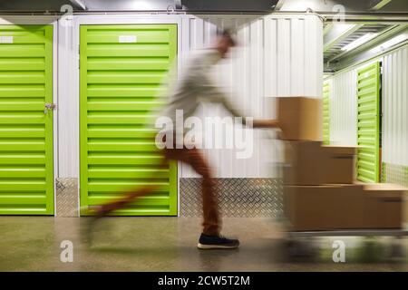 Cliché de mouvement flou d'un homme méconnaissable poussant un chariot avec des boîtes lorsqu'il court dans un espace de rangement autonome, dans un espace de copie Banque D'Images