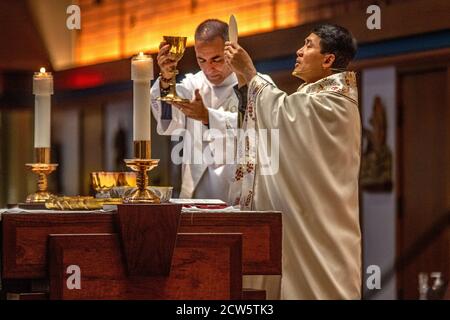 Portant des robes de cérémonie, un diacre tient un gobelet de vin sacramentel comme un prêtre américain asiatique tient le cadet de communion tout en dirigeant la masse à t Banque D'Images