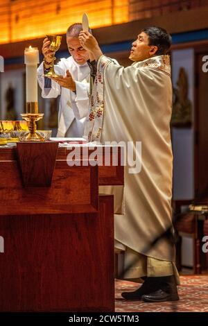 Portant des robes de cérémonie, un diacre tient un gobelet de vin sacramentel comme un prêtre américain asiatique tient le cadet de communion tout en dirigeant la masse à t Banque D'Images