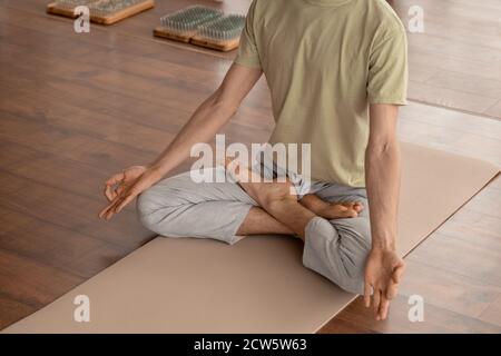Jeune homme en vêtements de sport gardant l'équilibre tout en étant assis sur un tapis en pose de lotus Banque D'Images