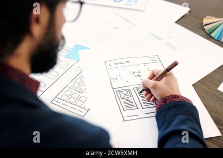 Main d'un jeune homme développeur d'application mobile tenant un crayon sur l'esquisse Banque D'Images