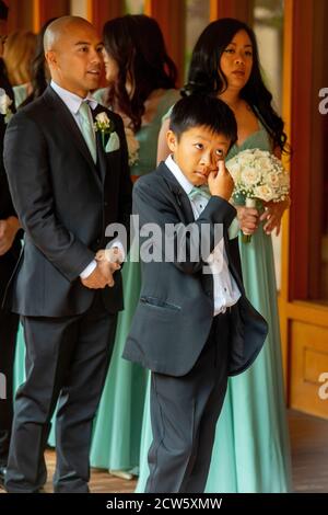 Portant un bouquet, les invités de mariage multiracial vêtus de façon formelle attendent d'entrer dans une église catholique de Californie du Sud. Banque D'Images