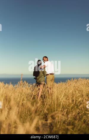 Vue arrière d'un couple romantique debout ensemble dans un champ. Portrait d'un couple en vacances appréciant la beauté de la nature. Banque D'Images