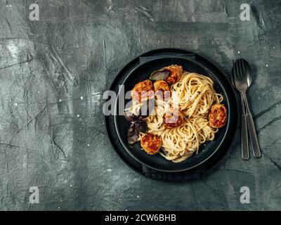 Boulettes de parmesan de courgettes aux pâtes Carbonara dans une assiette noire sur fond gris. Vue rapprochée de la carbonara crémeuse avec espace de copie restant. Vue de dessus ou plan de travail. Banque D'Images